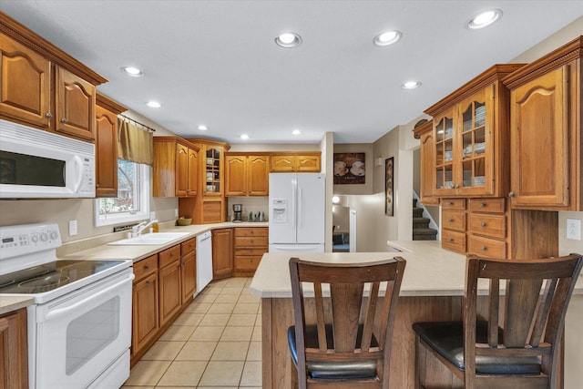 kitchen featuring a kitchen breakfast bar, sink, light tile patterned floors, and white appliances