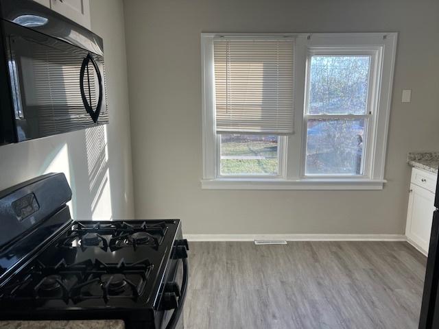 kitchen featuring light hardwood / wood-style floors, white cabinetry, a wealth of natural light, and black appliances