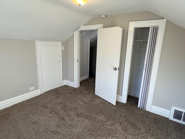 unfurnished bedroom with a closet, dark carpet, and vaulted ceiling