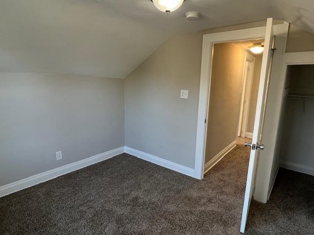 additional living space with dark carpet and vaulted ceiling