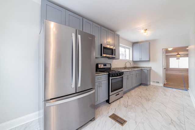 kitchen featuring appliances with stainless steel finishes, light stone counters, plenty of natural light, and gray cabinetry