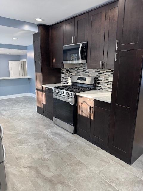 kitchen with dark brown cabinetry, stainless steel appliances, and tasteful backsplash