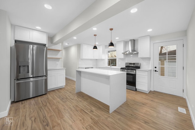 kitchen with pendant lighting, wall chimney range hood, light wood-type flooring, appliances with stainless steel finishes, and white cabinetry