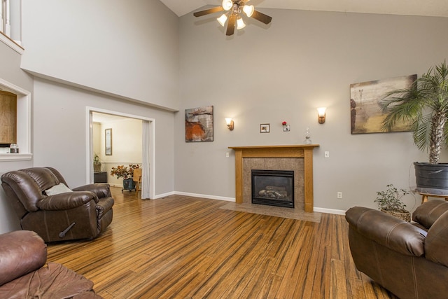 living room featuring ceiling fan, wood-type flooring, high vaulted ceiling, and a tiled fireplace