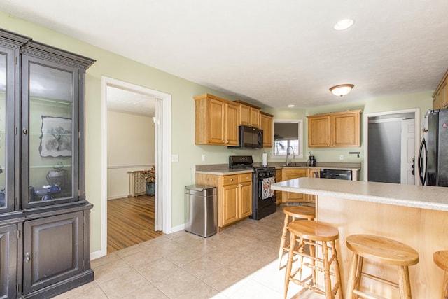 kitchen featuring light tile patterned floors, sink, a kitchen breakfast bar, and black appliances