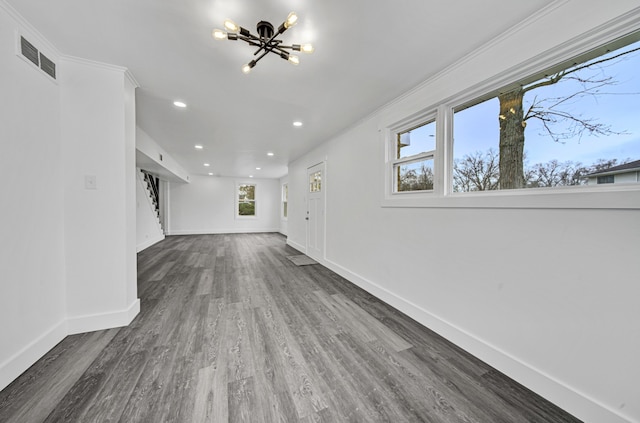 unfurnished living room with a notable chandelier, plenty of natural light, dark hardwood / wood-style flooring, and crown molding