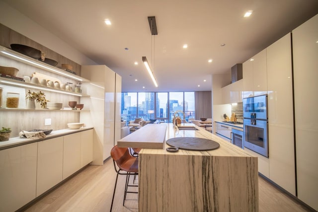 kitchen with a center island with sink, white cabinets, light hardwood / wood-style floors, and a wall of windows