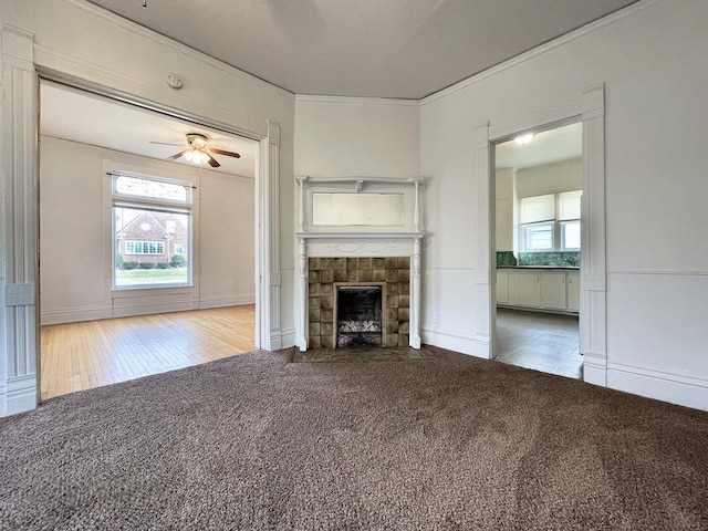 unfurnished living room featuring carpet flooring, ceiling fan, crown molding, and a tiled fireplace