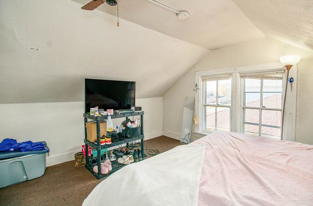 bedroom with ceiling fan, dark carpet, and vaulted ceiling