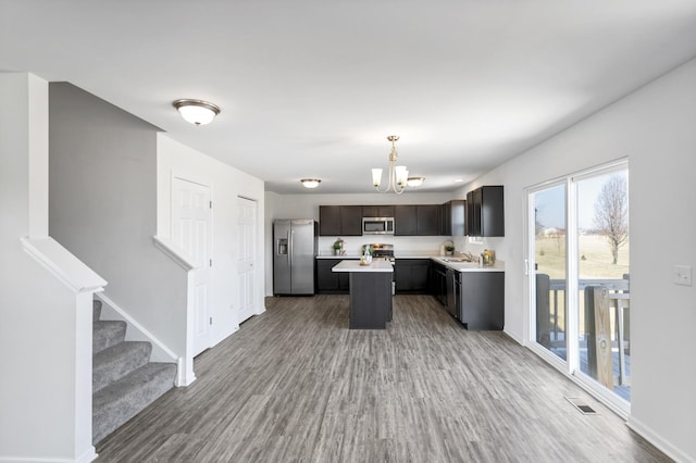 kitchen featuring wood-type flooring, appliances with stainless steel finishes, hanging light fixtures, a center island, and dark brown cabinetry