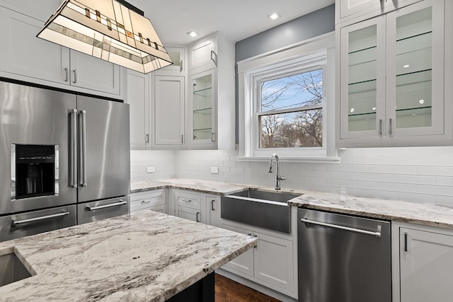 kitchen featuring light stone countertops, stainless steel appliances, sink, decorative light fixtures, and white cabinets