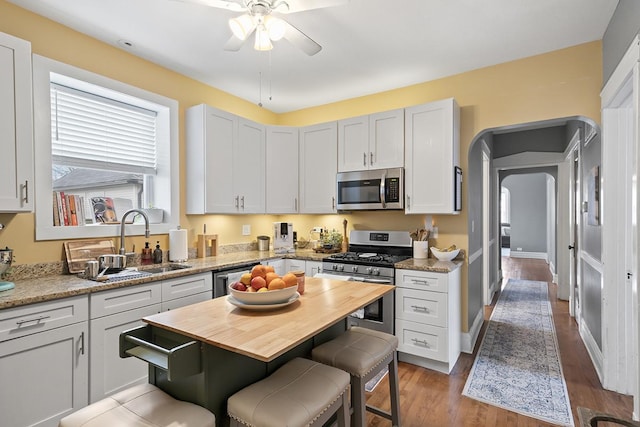 kitchen with white cabinetry, stainless steel appliances, light stone counters, and wood-type flooring