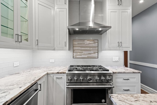 kitchen with backsplash, white cabinets, wall chimney exhaust hood, light stone counters, and stainless steel appliances