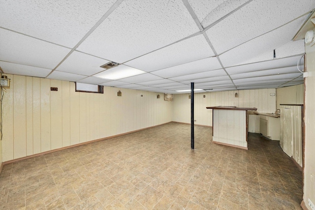 basement with a paneled ceiling and wooden walls