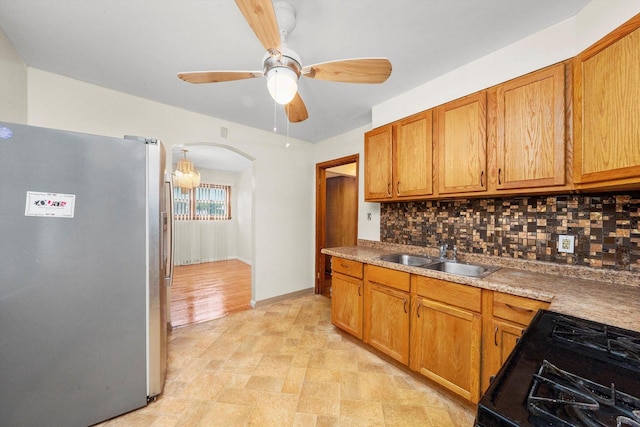 kitchen with stainless steel refrigerator, ceiling fan, sink, black gas range oven, and decorative backsplash