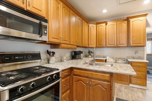 kitchen featuring light stone countertops, appliances with stainless steel finishes, light wood-type flooring, and sink