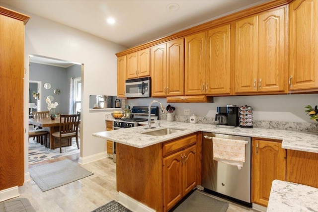 kitchen featuring light stone countertops, sink, appliances with stainless steel finishes, and light hardwood / wood-style flooring