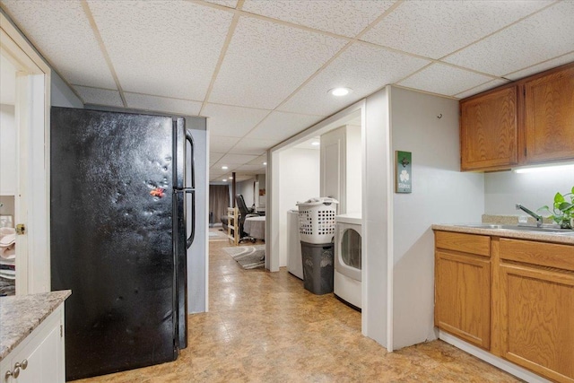 kitchen with washer / dryer, a paneled ceiling, black refrigerator, and sink