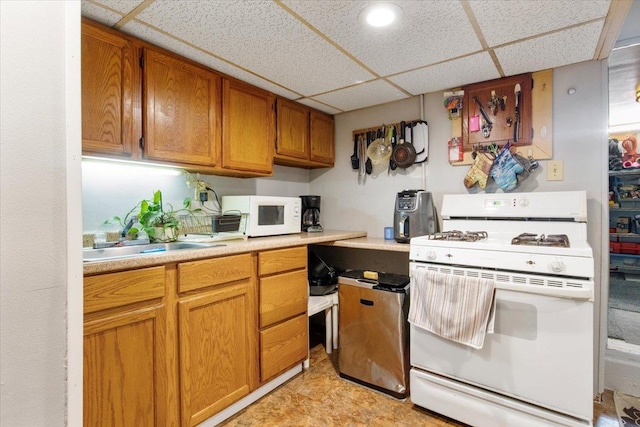 kitchen with a drop ceiling, white appliances, and sink