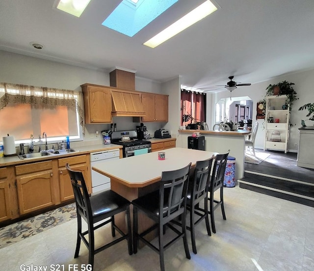 kitchen with white dishwasher, sink, ceiling fan, a kitchen island, and stainless steel range with gas stovetop