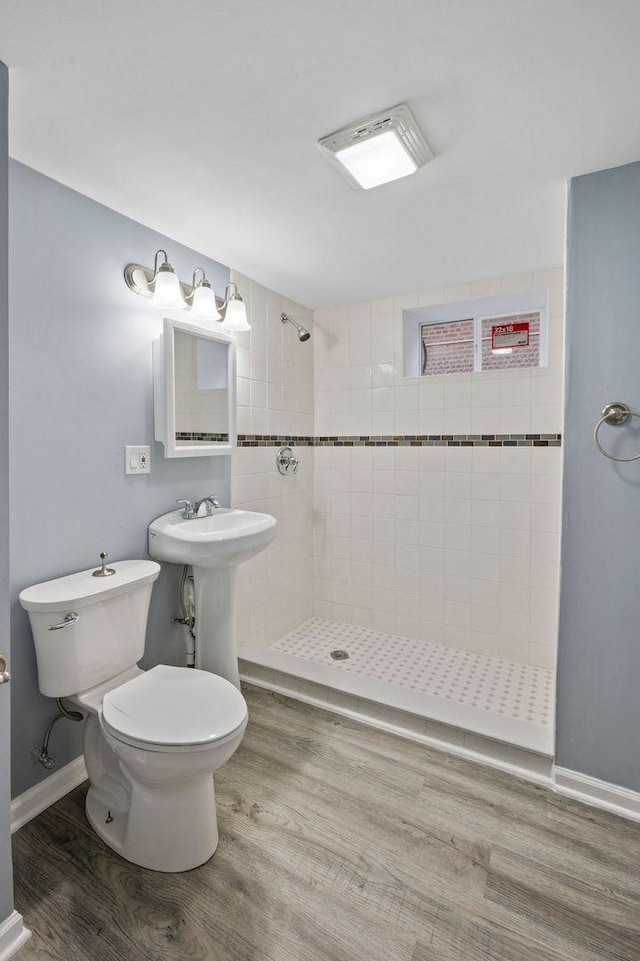 bathroom featuring toilet, hardwood / wood-style floors, a tile shower, and sink