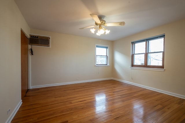 spare room featuring an AC wall unit, wood finished floors, a ceiling fan, and baseboards