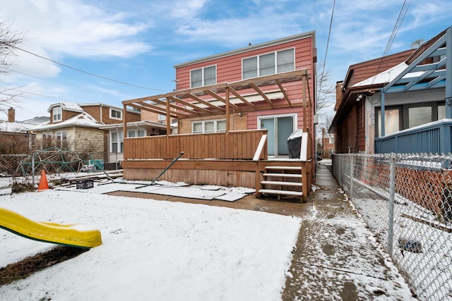 snow covered house featuring a playground, fence, and a wooden deck