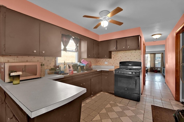 kitchen featuring black range with gas stovetop, decorative backsplash, ceiling fan, dark brown cabinetry, and kitchen peninsula