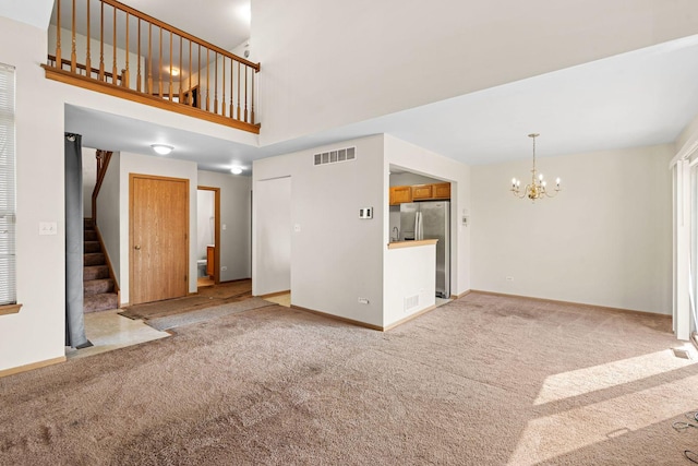 unfurnished living room featuring carpet, a notable chandelier, and a towering ceiling