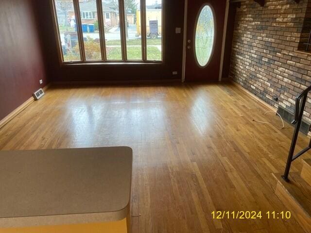 empty room with light wood-type flooring and brick wall