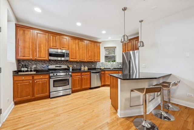 kitchen with pendant lighting, appliances with stainless steel finishes, backsplash, a kitchen bar, and light wood-type flooring