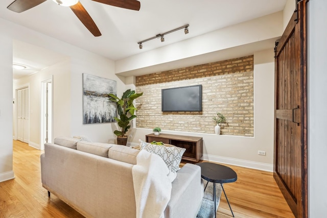 living room featuring brick wall, wood-type flooring, rail lighting, ceiling fan, and a barn door