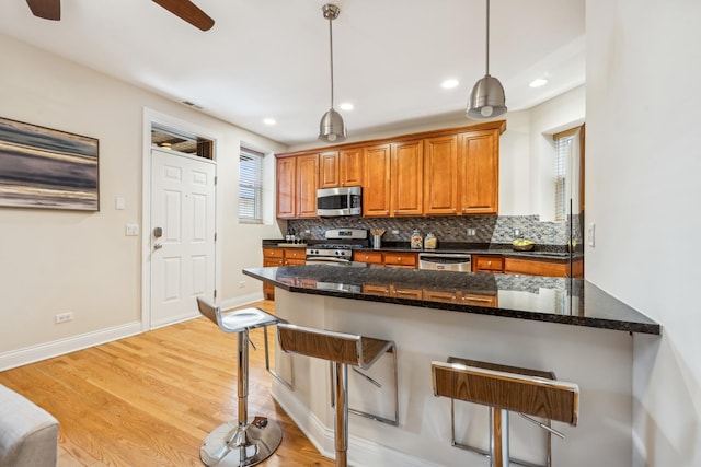 kitchen with a breakfast bar area, hanging light fixtures, backsplash, stainless steel appliances, and light hardwood / wood-style floors