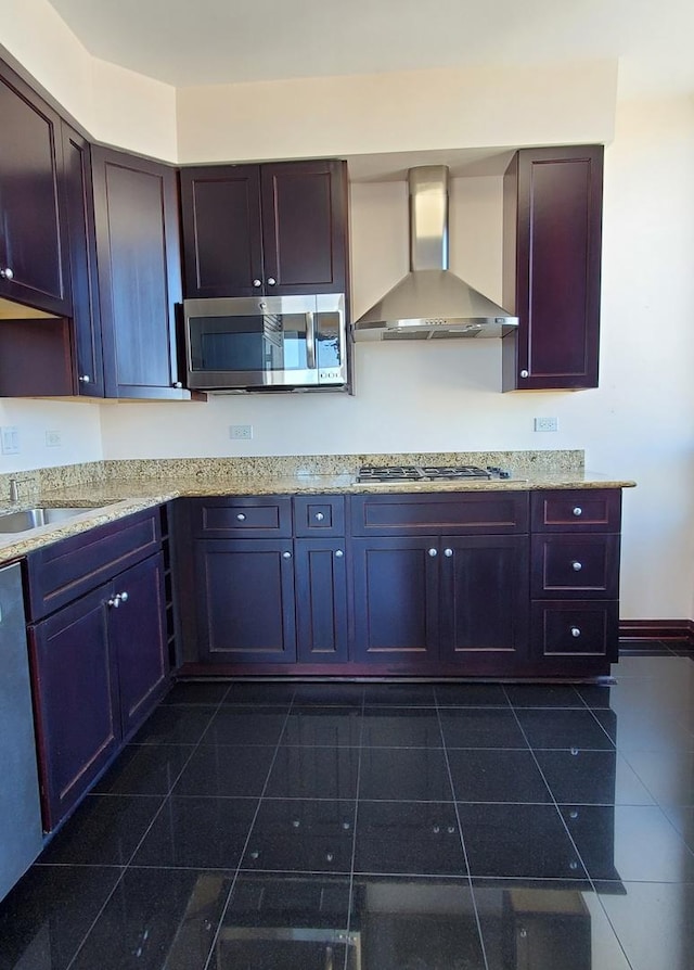 kitchen featuring appliances with stainless steel finishes, wall chimney range hood, light stone counters, and sink