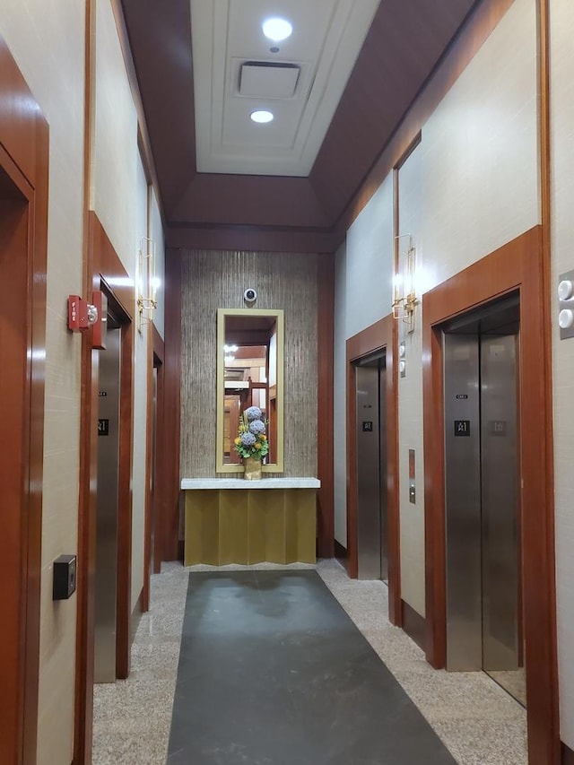 hall with elevator, light colored carpet, and a tray ceiling