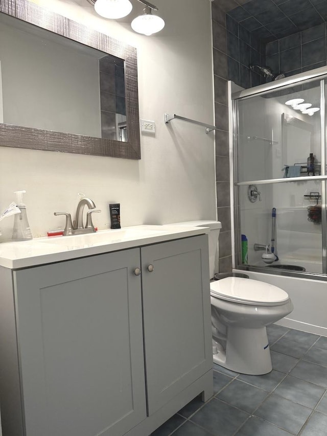 full bathroom with bath / shower combo with glass door, toilet, vanity, and tile patterned flooring