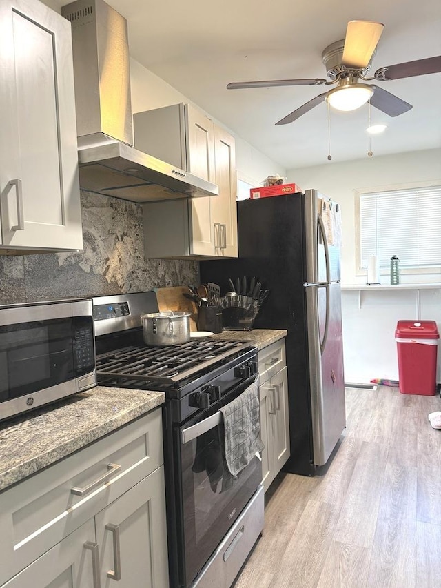 kitchen featuring light wood-style flooring, backsplash, appliances with stainless steel finishes, wall chimney exhaust hood, and light stone countertops