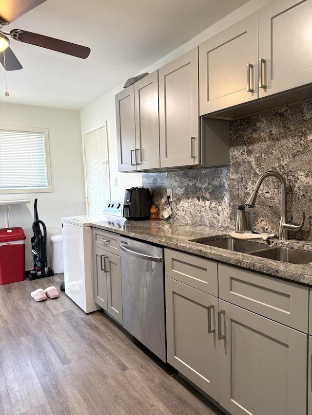 kitchen with backsplash, gray cabinetry, stainless steel dishwasher, wood finished floors, and a sink