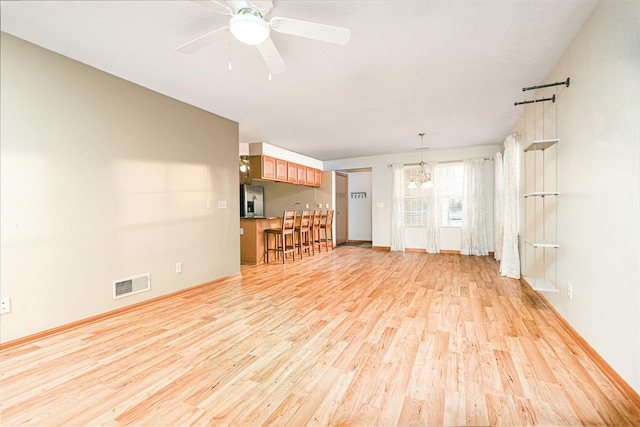 unfurnished living room featuring ceiling fan with notable chandelier and light hardwood / wood-style floors