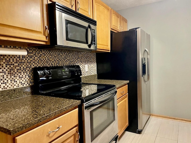 kitchen featuring appliances with stainless steel finishes, backsplash, light tile patterned floors, and dark stone countertops