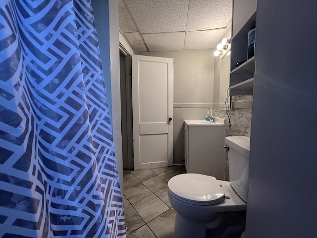 bathroom with a paneled ceiling, tile patterned flooring, vanity, and toilet