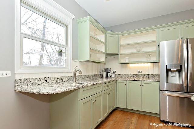 kitchen with stainless steel fridge with ice dispenser, green cabinetry, light hardwood / wood-style flooring, and light stone countertops