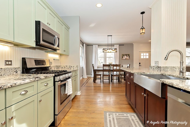 kitchen featuring light hardwood / wood-style floors, light stone countertops, appliances with stainless steel finishes, sink, and pendant lighting