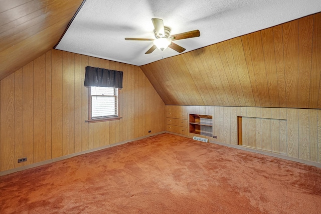 bonus room featuring lofted ceiling, wooden walls, carpet floors, and a textured ceiling