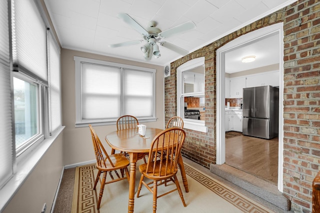 dining room featuring ceiling fan, light hardwood / wood-style floors, ornamental molding, and brick wall