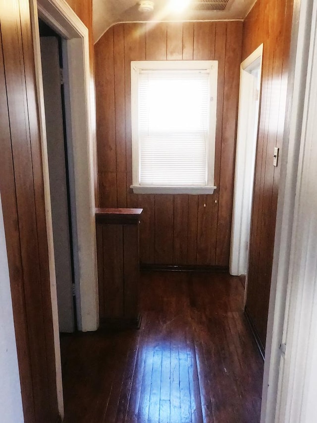 hallway featuring dark wood-type flooring, lofted ceiling, and wood walls