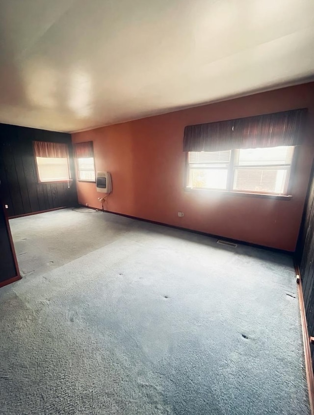 empty room featuring carpet flooring, heating unit, and wooden walls