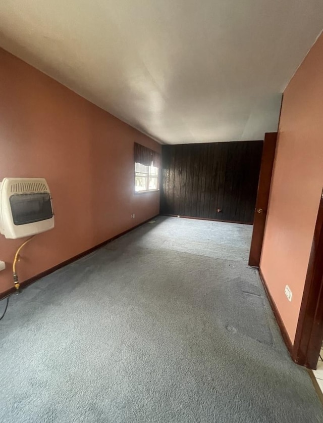 carpeted empty room featuring heating unit and wood walls