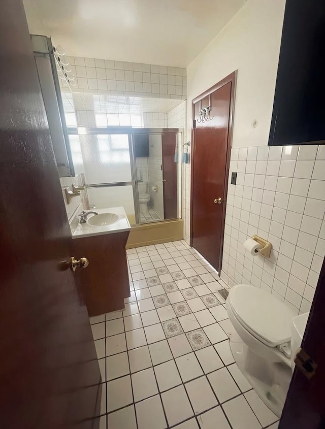 bathroom with tile patterned floors, vanity, tile walls, toilet, and a shower with shower door