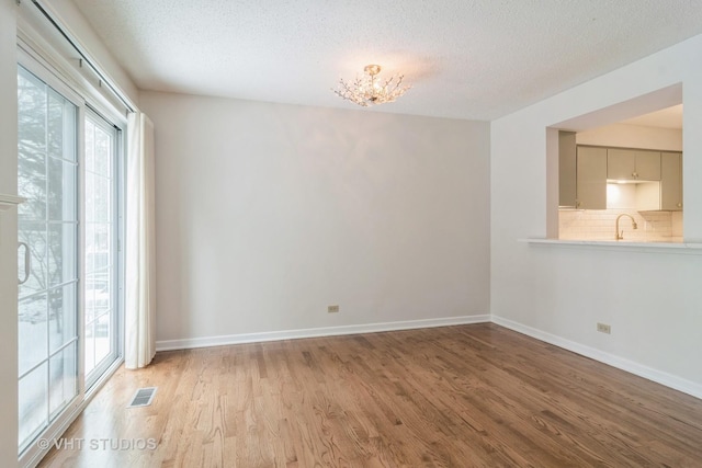 empty room featuring sink, light hardwood / wood-style flooring, a textured ceiling, and a notable chandelier